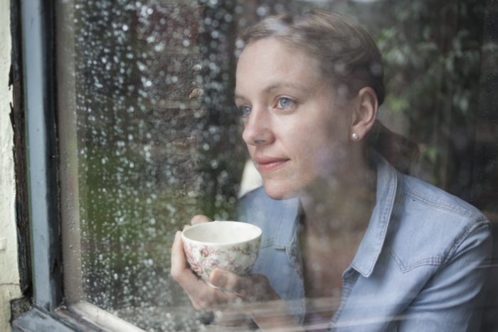 Nadine Petry hinter einer verregneten Fensterscheibe mit einer Tasse Tee