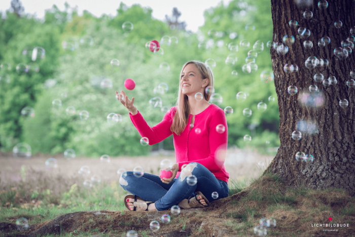 Nadine Petry sitzt jonglierend unter einem Baum. Im Vordergrund sind Seifenblasen.
